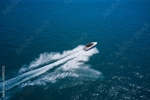 Big speedboat fast moving on blue water diagonally aerial view. White boat with people on blue water top view.