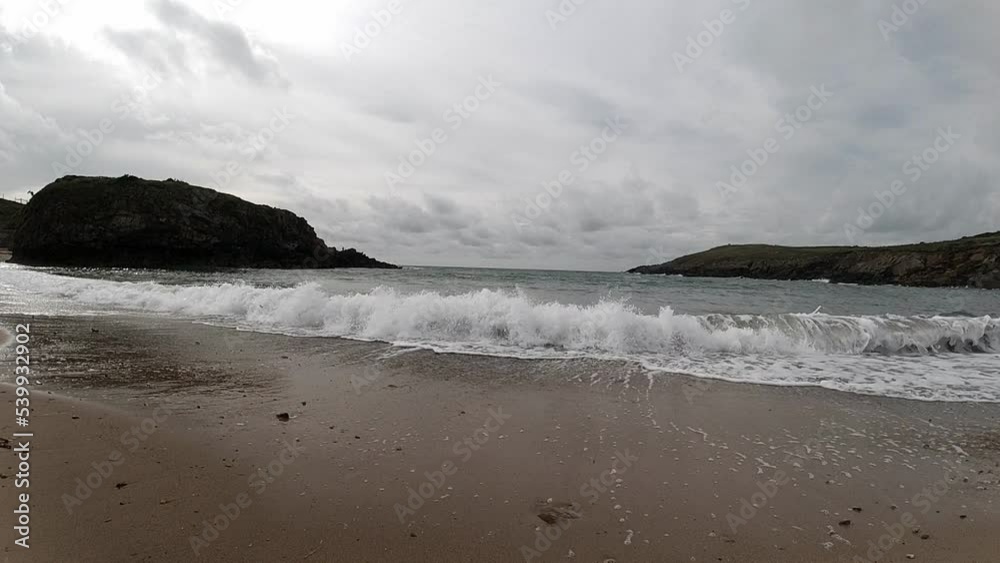 Slow motion tide crashing on sandy beach with island mountains across horizon Slow motion tide crashing on sandy beach with island mountains across horizon