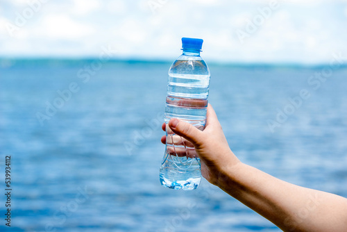 A girl holds a bottle of drinking water in her hand against a blue sky background 