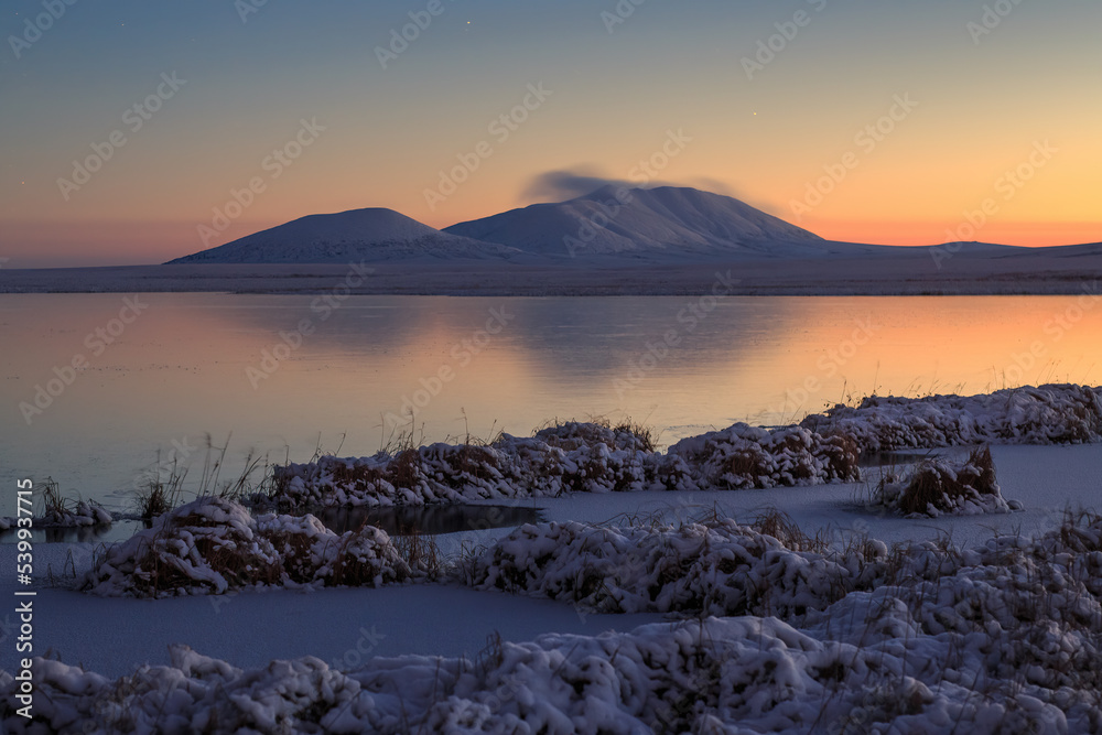 Beautiful evening arctic landscape. View of the mountain and the frozen lake in the snow-covered tundra. Cold autumn in the polar region. October in the Arctic. Frosty weather. Harsh northern nature.
