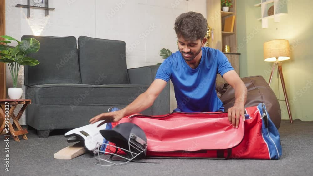 happy young cricketer packing his accessories kit for playing or practicing match at home - concept of sportsman, athlete and hobby or leisure activities