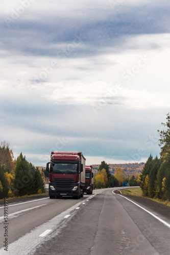 Autumn landscape. On the freeway. Travel by car. A truck is moving along the freeway. Beautiful autumn forest around the road. Nature of Eastern Siberia. Vertical photo.