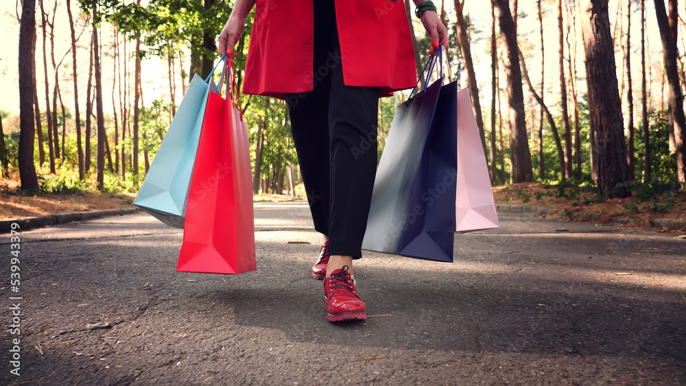 woman with shopping bags. female legs in red shoes, close-up. Woman with colored shopping bags in her hands, walking through city park. shopping and gifts. delivery or donation concept. High quality