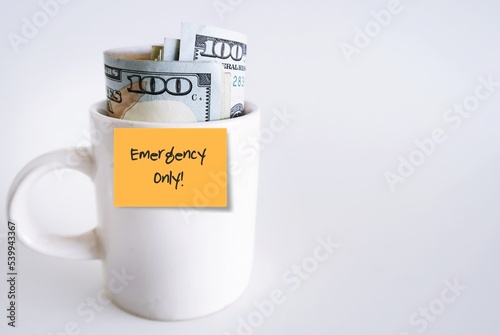 Wallpaper Mural White ceramic cup with cash dollars money with orange paper stick note written EMERGENCY ONLY, isolated on white background. smart financial planning to save money for contingency fund - for rainy day Torontodigital.ca