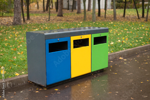 Three different garbage container for sorting waste in the park. Yellow for plastic, green for glass, blue for paper. Separating and sorting trash, concept pollution of the environment.