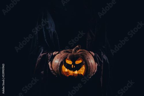Fototapeta The witch is holding a pumpkin jack o lantern glowing in the dark