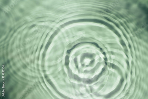 Defocused rippled transparent green water gel with concentric expanding circles on surface from fallen drop with waves