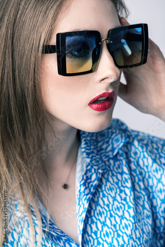 Fashion and style concept. Close-up retro woman style portrait with big colorful sunglasses and vivid makeup with red lipstick wearing blue blouse. Selective focus. Eyes is in camera focus