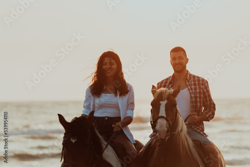 A loving couple in summer clothes riding a horse on a sandy beach at sunset. Sea and sunset in the background. Selective focus 