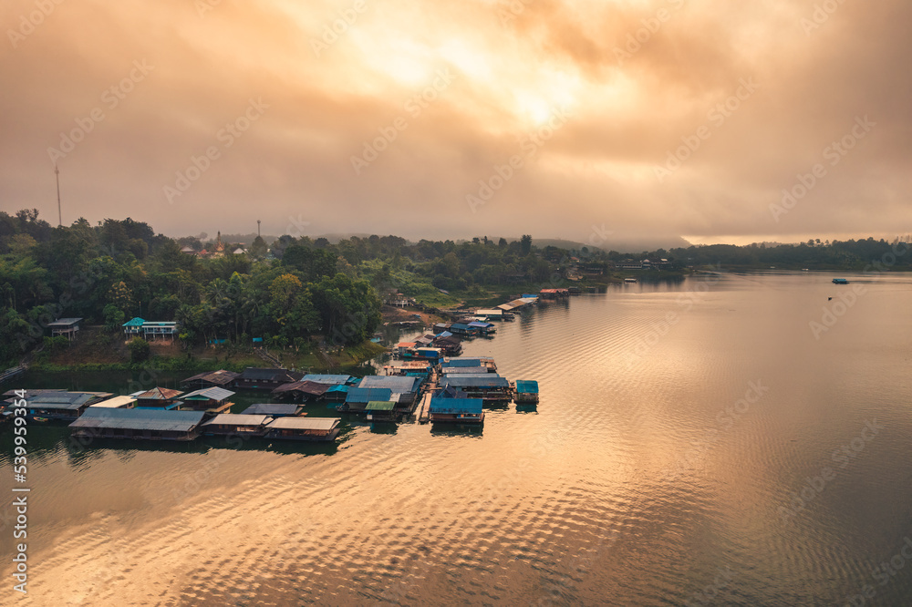 Golden sunrise over local traditional Mon village floating with foggy in the dam at the morning in Sangkhlaburi
