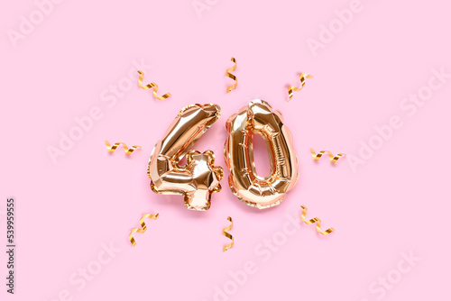 Number fourty golden foil balloons with ribbon confetti on a pink pastel background.