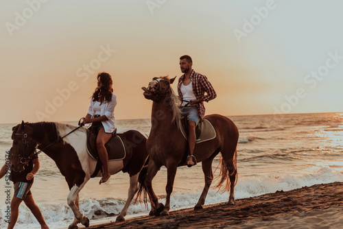 A loving couple in summer clothes riding a horse on a sandy beach at sunset. Sea and sunset in the background. Selective focus 