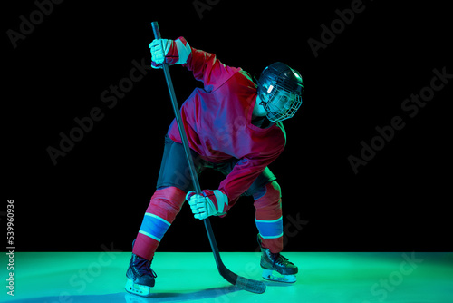 Photography Junior ice hockey player in sports uniform and protective equipment in action over dark background in neon light