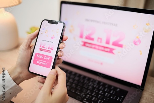 Online Shopping Website on Laptop. Easy E-commerce Website Shop by Smartphone, iPhone, iPad and Laptop. Close up Hands Using Smartphone Shopping online with promo code. 12.12 promotion sale.