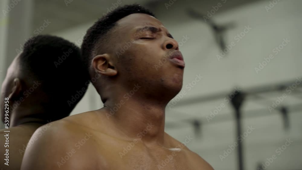 Shirtless muscular young black man taking a break by mirror at the gym