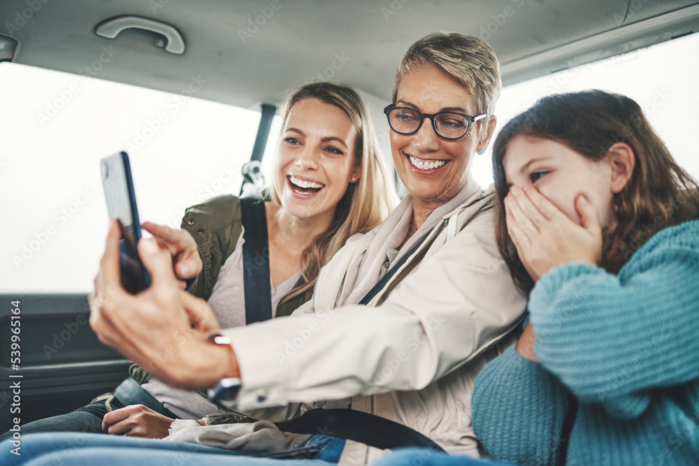 Family, phone and women taking a selfie in the car on road trip adventure. Grandmother, mom and girl smile for picture on smartphone in backseat for memories of holiday, journey and vacation weekend Family, phone and women taking a selfie in the car on road trip adventure. Grandmother, mom and girl smile for picture on smartphone in backseat for memories of holiday, journey and vacation weekend