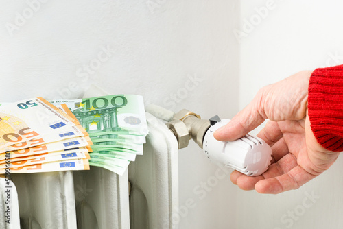 Male hand adjusting home gas heater - Euro banknotes on house radiator with man lowering the temperature valve - Concept of expensive energy costs due sanctions and geopolitical events - Image