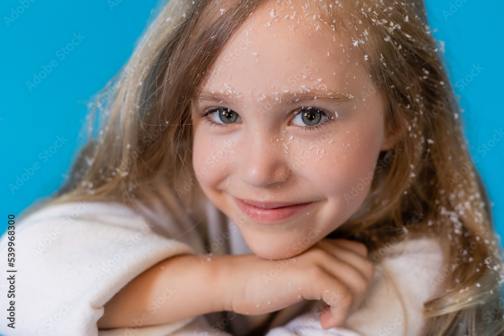 portrait of a cute little blonde girl in a white knitted sweater on a blue background in the studio. snowflakes in the hair, the concept of winter portrait of a cute little blonde girl in a white knitted sweater on a blue background in the studio. snowflakes in the hair, the concept of winter
