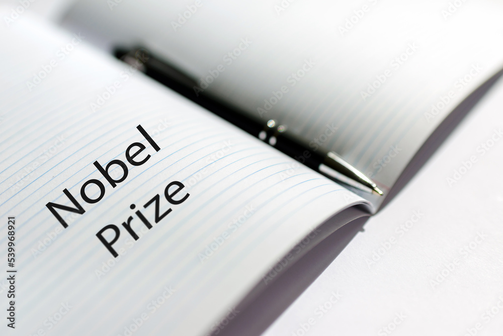 The inscription NOBEL PRIZE on a white sheet notebook.Nobel prize in literature. A pen is lying nearby.White background.Selective focus,close-up. The inscription NOBEL PRIZE on a white sheet notebook.Nobel prize in literature. A pen is lying nearby.White background.Selective focus,close-up.