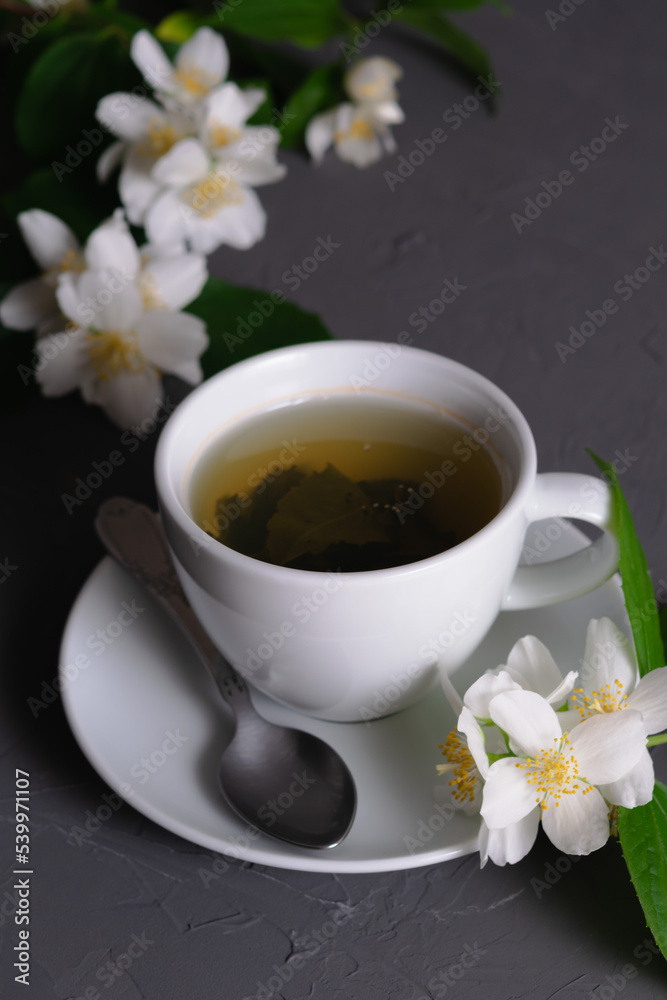 White porcelain cup with fragrant green tea and blooming jasmine on a gray background. Close-up. Time for tea. White porcelain cup with fragrant green tea and blooming jasmine on a gray background. Close-up. Time for tea.