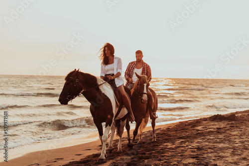 A loving couple in summer clothes riding a horse on a sandy beach at sunset. Sea and sunset in the background. Selective focus 