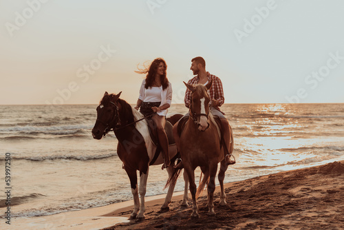A loving couple in summer clothes riding a horse on a sandy beach at sunset. Sea and sunset in the background. Selective focus 