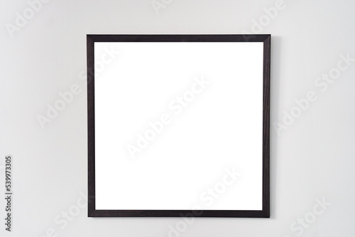 An empty square photo frame with a black border hanging on a white wall. High quality photo