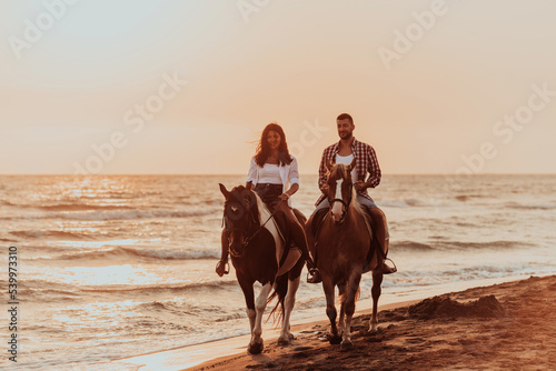 A loving couple in summer clothes riding a horse on a sandy beach at sunset. Sea and sunset in the background. Selective focus 