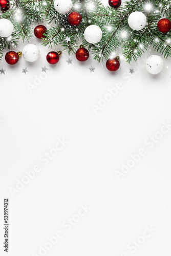 Christmas snow border of shiny white and red balls, evergreen branches on a white wooden background. New year card