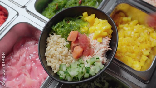 Poke Bowl With Rice Topped With Cucumber, Limu, Maui Onions, Ripe Mangoes, And Uncooked Tuna And Salmon Fish. close up photo