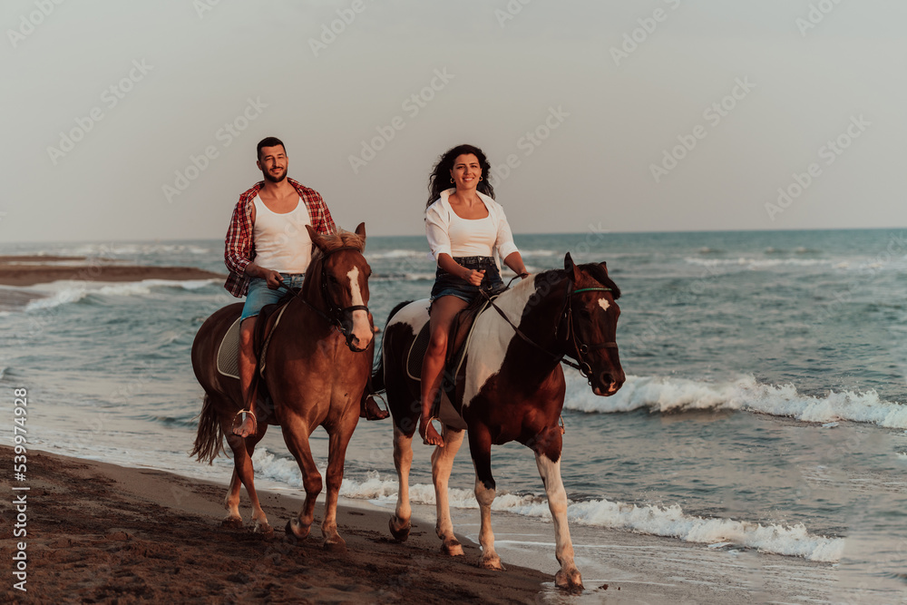 A loving couple in summer clothes riding a horse on a sandy beach at sunset. Sea and sunset in the background. Selective focus A loving couple in summer clothes riding a horse on a sandy beach at sunset. Sea and sunset in the background. Selective focus