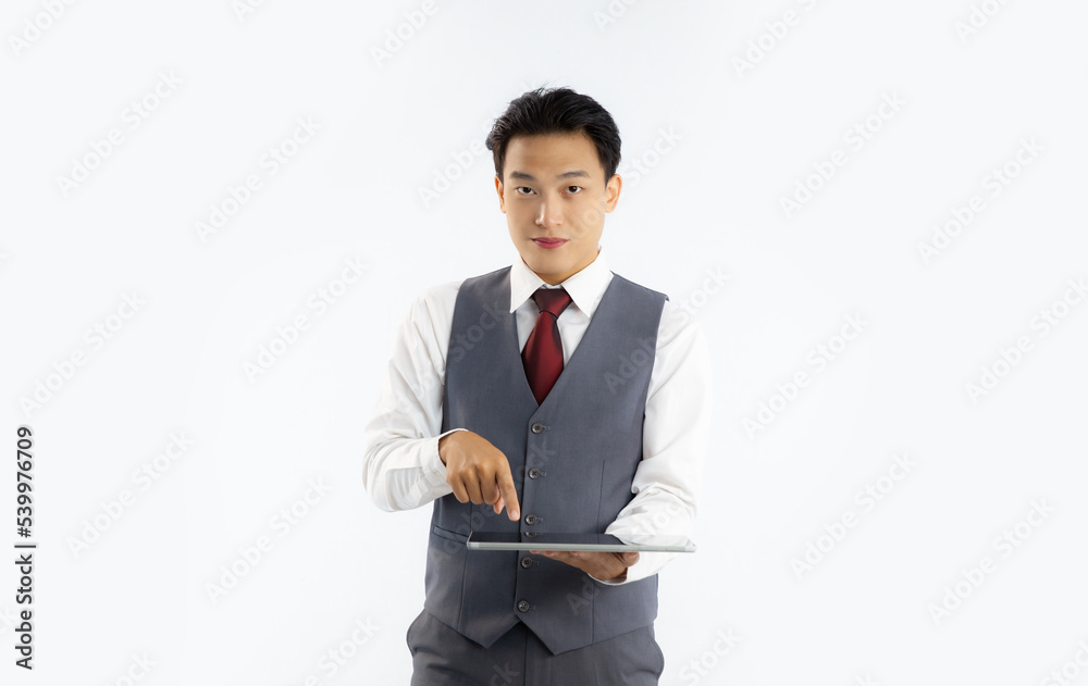 Young asian businessman in grey vest suit white shirt red tie holding tablet touching screen looking camera white background.
Young asian businessman in grey vest suit white shirt red tie holding tablet touching screen looking camera white background.
