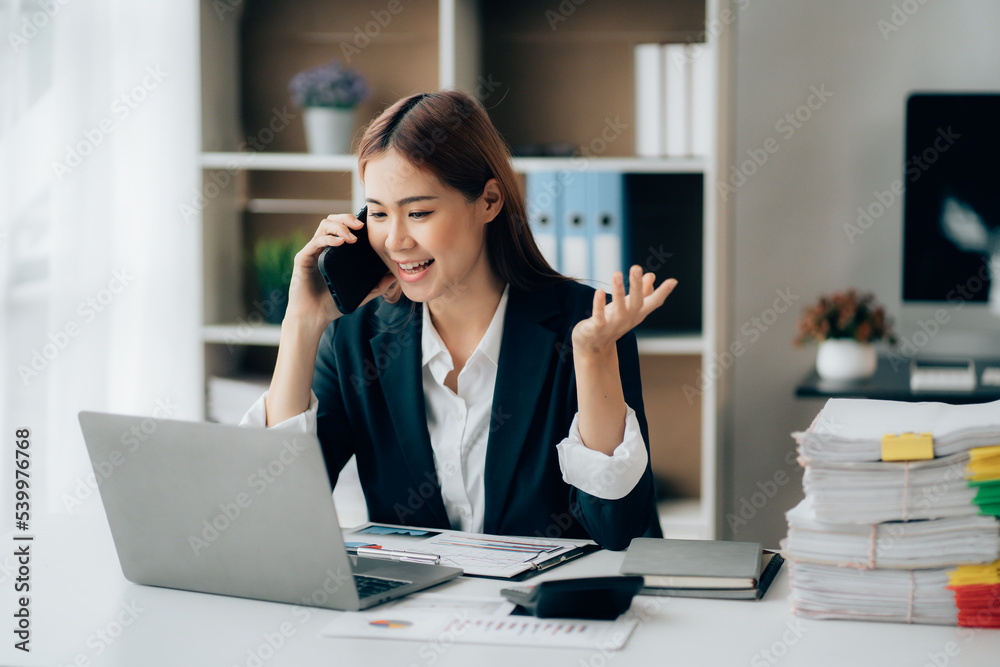 Asian businesswoman talking on phone, using laptop, looking at screen, entrepreneur manager consulting client by call, looking at computer screen, discussing project, reading information