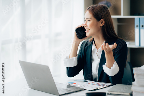 Asian businesswoman talking on phone, using laptop, looking at screen, entrepreneur manager consulting client by call, looking at computer screen, discussing project, reading information