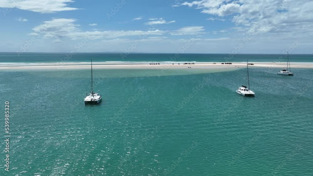 Flying over the water between catamaran boats towards vehicles parked on sandbar Flying over the water between catamaran boats towards vehicles parked on sandbar