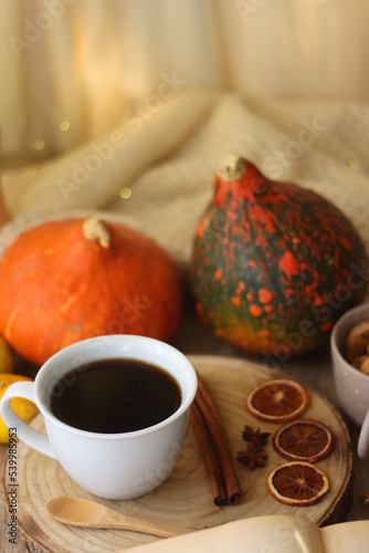 Cup of tea or coffee  seasonal spices  bowl of cookies  blanket  pumpkins  colorful leaves  books and tangerines on wooden table. Cozy hygge at home. Selective focus.