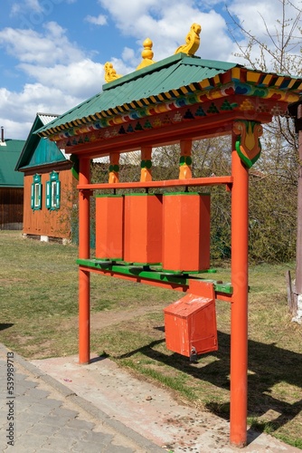 Bright orange wooden Buddhist prayer wheels and a donation box on the territory of the Ivolginsky Datsan. Russia, Republic of Buryatia, Verkhnyaya Ivolga village, May 12, 2022 © ok_fotoday