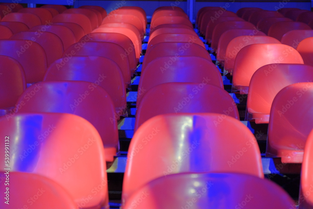 Naklejka premium red plastic grandstand chairs under blue light
