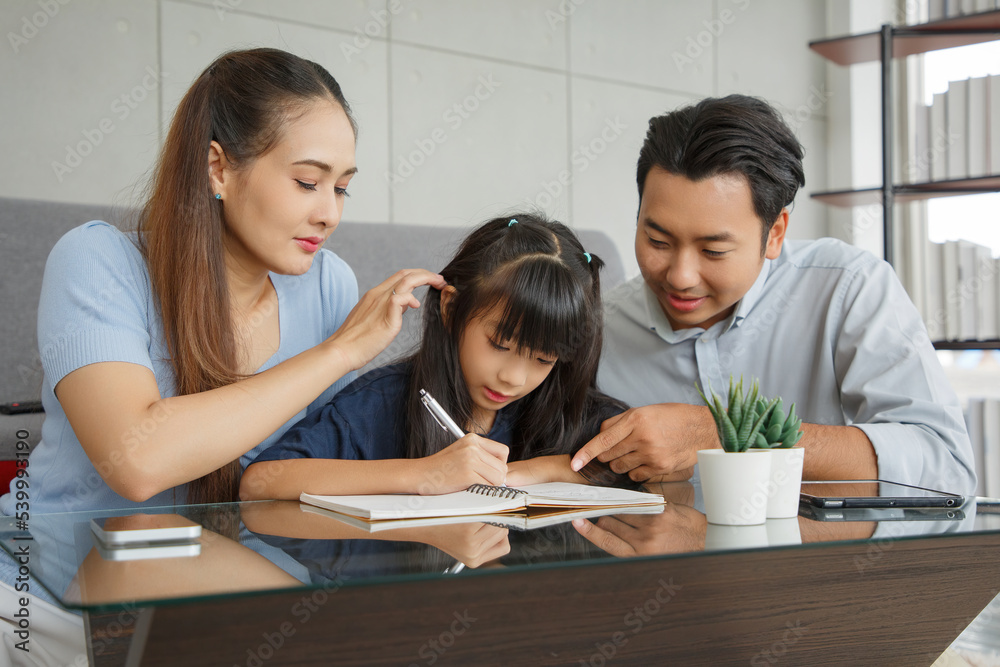 Children education and home school concept : Young asian father and mother see little daughters' study. Excited smiling small child girl enjoying learning and writing with pleasant dad and mom at home Children education and home school concept : Young asian father and mother see little daughters' study. Excited smiling small child girl enjoying learning and writing with pleasant dad and mom at home