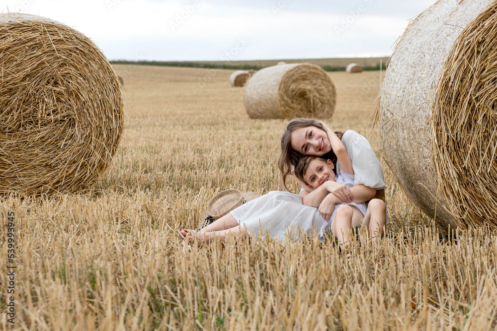 Young mother and her son are hugging near straw bales in a field. A happy family. Mother's day Young mother and her son are hugging near straw bales in a field. A happy family. Mother's day