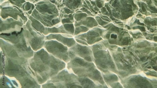 Rippling water surface with light reflection and floating small fish under water. A view of the bottom of sea through the water surface with rippling light and waves.