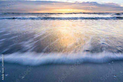фотографія Scenic shot of a white foamy waves on the beach during the sunset