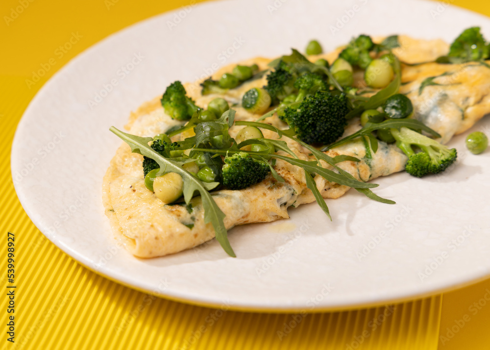 amlet with egg and greens on a white plate on a yellow background amlet with egg and greens on a white plate on a yellow background