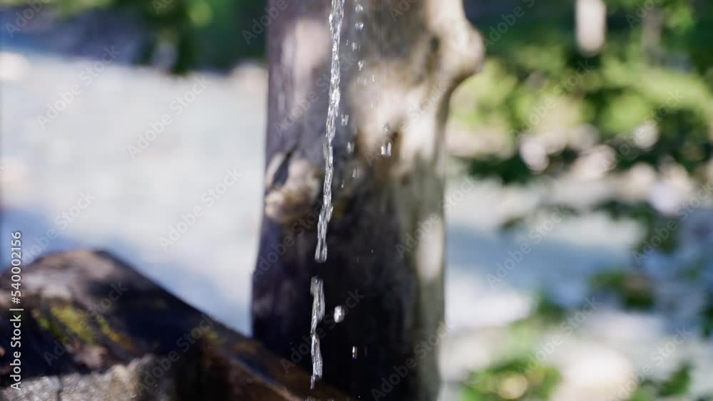 Fountain water flowing out of wooden log hollow into old trough in slow motion, tracking shot Fountain water flowing out of wooden log hollow into old trough in slow motion, tracking shot