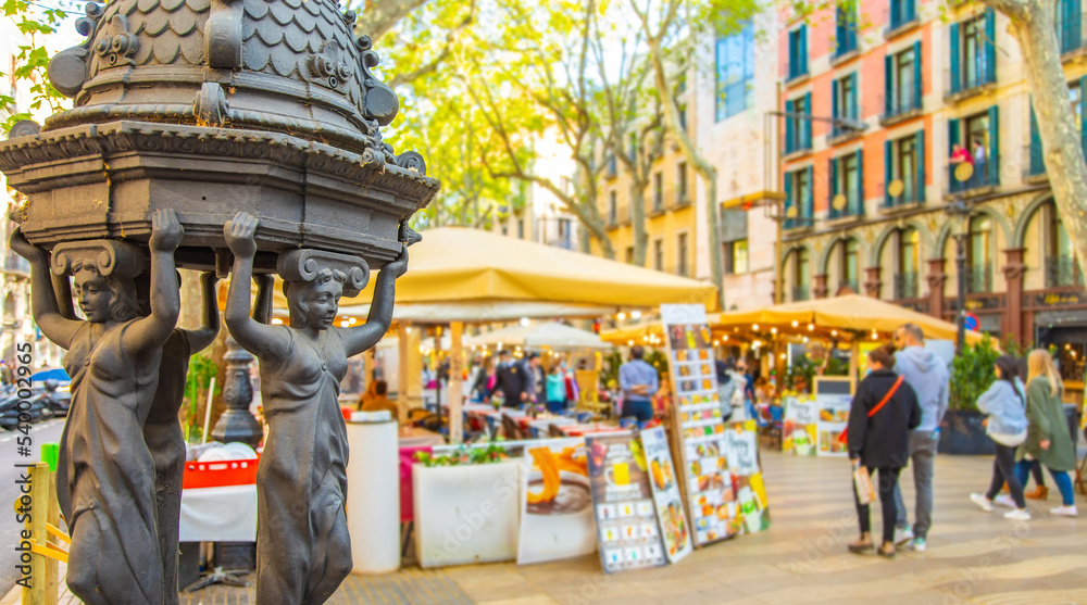 La Rambla most popular pedestrian street in Barcelona. Selective focus on drinking water fountain on foreground.