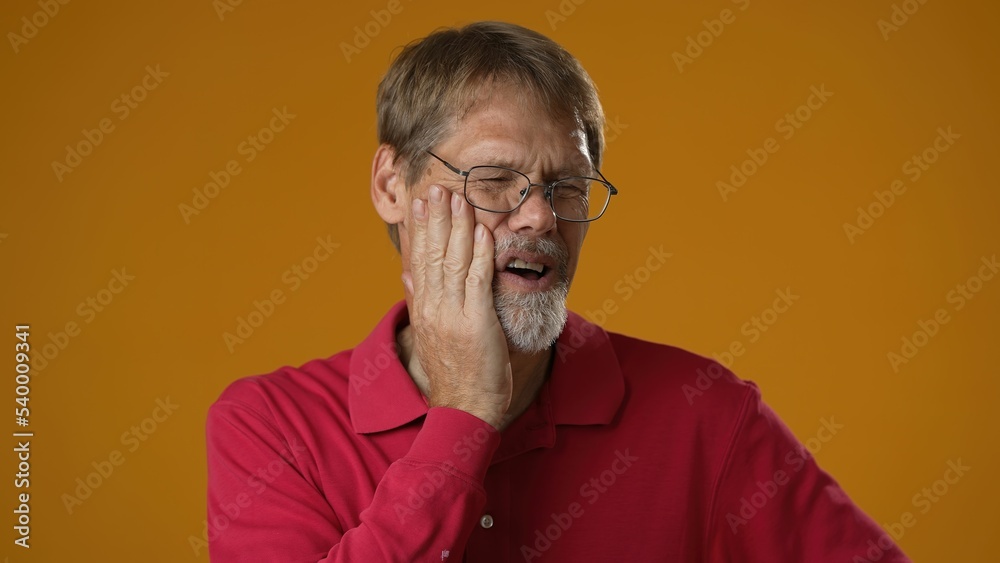 Mature handsome man in red shirt with tooth pain on yellow studio background. Male suffering from tooth ache, touching cheek, pulp inflammation, gingivitis Mature handsome man in red shirt with tooth pain on yellow studio background. Male suffering from tooth ache, touching cheek, pulp inflammation, gingivitis