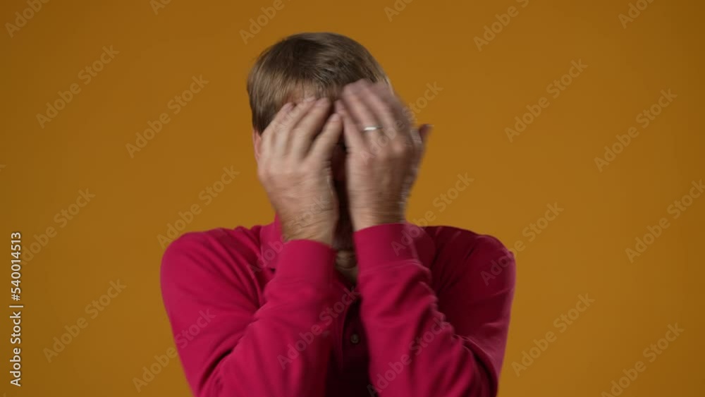 Shocked surprised mature man covers eyes with hands isolated on solid yellow background. Shocked surprised mature man covers eyes with hands isolated on solid yellow background.
