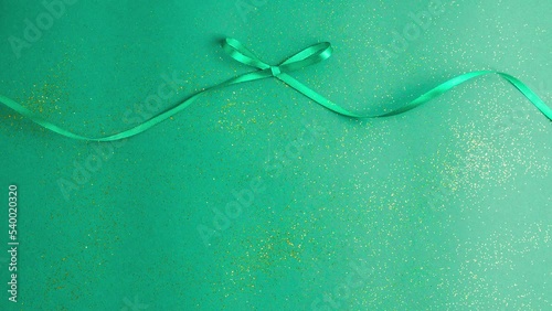Emerald green satin ribbon bow that tied and untied on green with gold colored glitter. Stop motion animation Christmas Holidays and presents concept flat lay with copy space