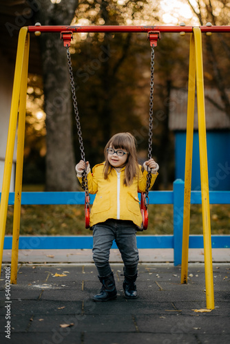 Happy child with down syndrome enjoying swing on playground