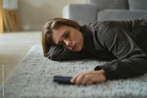 Caucasian nervous woman lying down on the floor and waiting for message photo